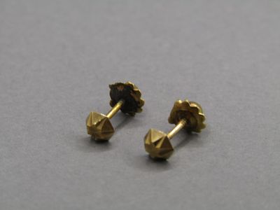 une paire de petites boucles d'oreilles en or sur un fond gris