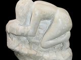 a white sculpture of a person sitting on a rock