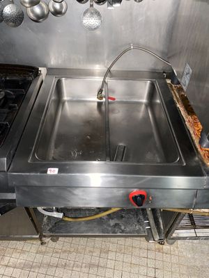 un évier en acier inoxydable dans une cuisine professionnelle, avec des casseroles et des poêles accrochées au mur