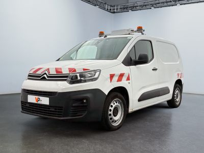 La camionnette blanche est garée dans une grande pièce ; elle porte une bande rouge et blanche sur le côté.
