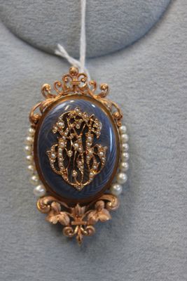 une photo d'une broche bleue et dorée ornée de perles, montée sur un collier