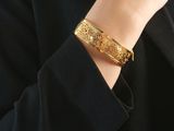 a close up of a person wearing a gold bracelet and a black jacket