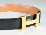 black leather belt with gold h buckle on a white surface