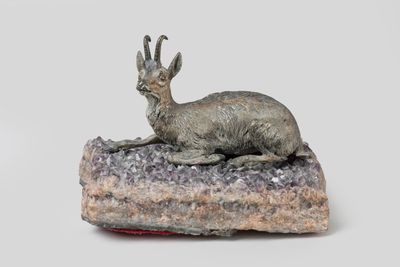 statue of a goat laying on a rock on a white background