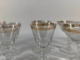 four glass goblets with gold rims are lined up on a table