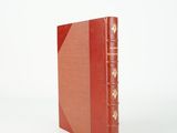 an old book with a red cover sitting on top of a white surface