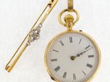 une montre de poche en or et une pince à cravate posées sur une surface blanche