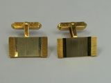 two gold cufflinks with black stripes on them on a white surface