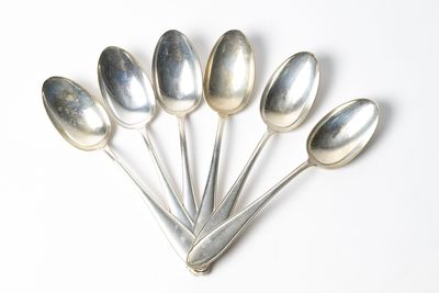 six cuillères en argent sont disposées en ligne sur une surface blanche