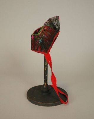 un petit chapeau rouge posé sur un support noir, orné d'un ruban rouge