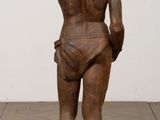 statue of a woman standing on a wooden platform with a white wall in the background