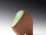 un petit objet marron avec une partie supérieure verte, posé sur une surface blanche