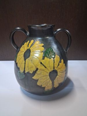 un vase noir orné de fleurs jaunes, posé sur une table
