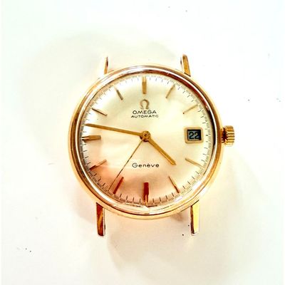 une montre en or avec un cadran blanc posée sur une surface blanche