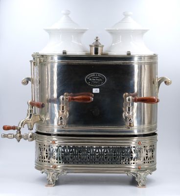 une cafetière ancienne en métal argenté, surmontée de deux tasses