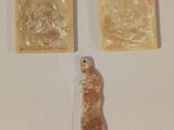 Trois œuvres d'art sont exposées sur une surface blanche ; l'une d'entre elles représente une femme et une autre un homme.