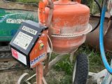 une bétonnière orange garée dans la cour, à côté d'une roue verte
