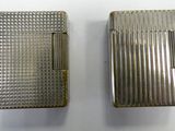 two silver cigarette cases sitting next to each other on a white surface