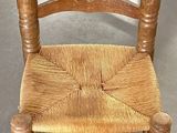 une petite chaise en bois avec une assise tressée, posée par terre