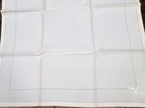 une serviette en lin blanche bordée d'une frange blanche, posée sur une table en bois