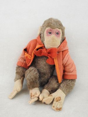 un singe en peluche portant une veste orange, assis sur une surface blanche