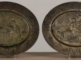 pair of bronze plates with figures on them sitting on a table