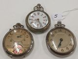 Trois montres de poche anciennes sont exposées sur un support blanc