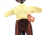 une poupée qui porte un pull jaune et un pantalon marron