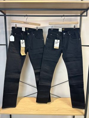 deux paires de jeans noirs suspendues à un portant dans un magasin