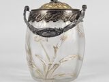an antique glass jar with a metal lid and a flower design