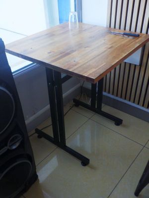 une table avec un plateau en bois et des pieds noirs, placée devant une fenêtre