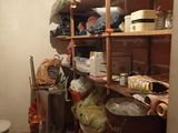 a room with a toilet, a trash can and a shelf full of items