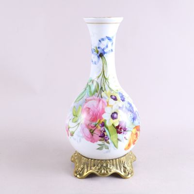 un vase blanc orné de fleurs peintes, posé sur un socle doré