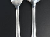 two silver spoons and a fork on a black table