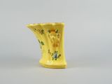 yellow vase with flowers and birds on it sitting on a table