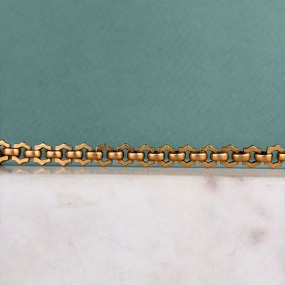 un gros plan d'un bracelet à chaîne en or posé sur une surface en marbre