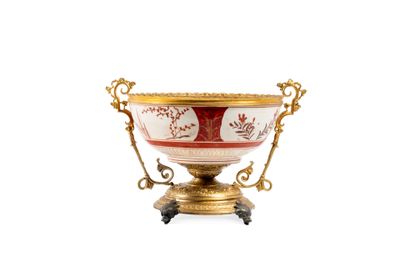 un bol richement décoré, doré et rouge, posé sur un socle, sur fond blanc