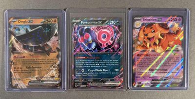 trois cartes Pokémon différentes, rangées dans des pochettes en plastique, posées sur une table