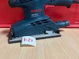 un gros plan d'une ponceuse filaire posée sur une table, avec une boîte rouge en arrière-plan
