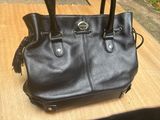 black leather handbag with tassels on top of it on a wooden table