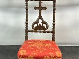 une vieille chaise en bois avec une assise rembourrée rouge et une croix sur le dossier