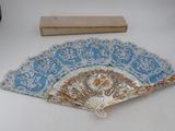 a blue and white fan with gold designs on it next to a ruler