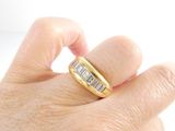 a man ' s hand holding a gold ring with baguets on it