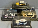 Quatre maquettes d'ambulances différentes sont exposées dans une vitrine posée sur une table