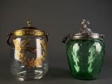 two green glass jars with gold designs and lids on a gray surface