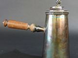 an antique silver coffee pot with wooden handle on a black surface