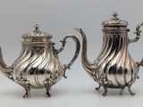 pair of silver plated teapots on stand on grey background