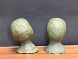 pair of bronze head sculptures on wooden table against black wall