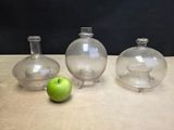 three glass vases sitting on a table with an apple in front of them