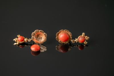 une paire de boucles d'oreilles en corail et or posées sur un fond noir